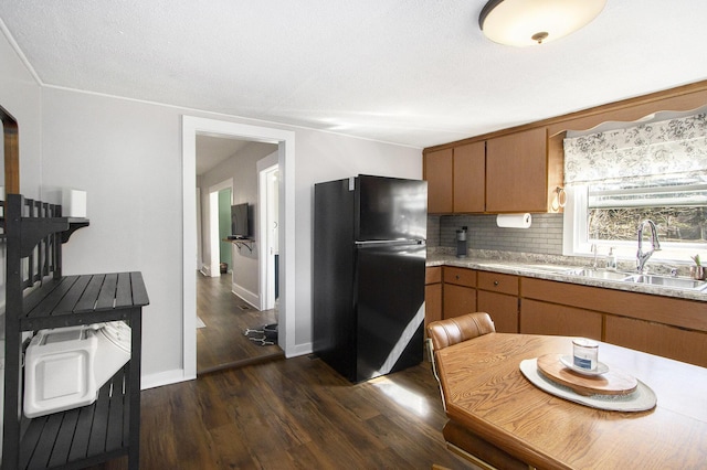 kitchen with dark wood-style floors, brown cabinets, freestanding refrigerator, and a sink