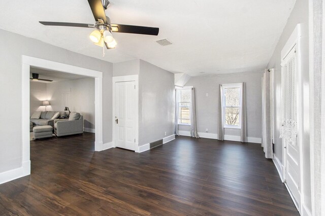 living area featuring visible vents, baseboards, a ceiling fan, and dark wood-style flooring