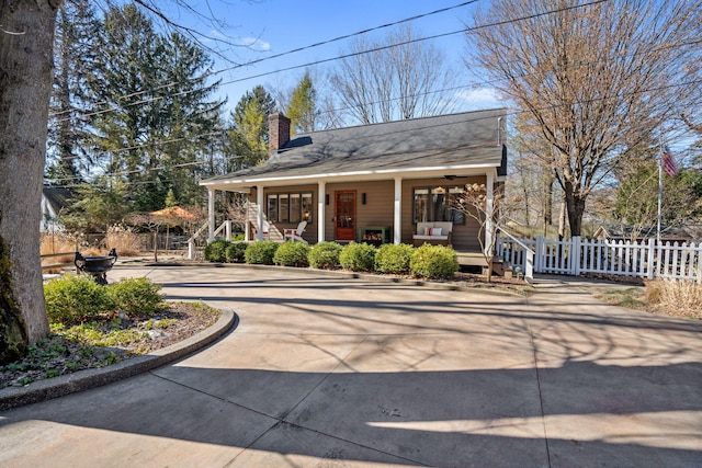 exterior space featuring a porch, a chimney, driveway, and fence