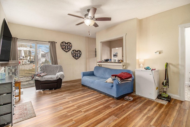 living area featuring baseboards, ceiling fan, and light wood finished floors