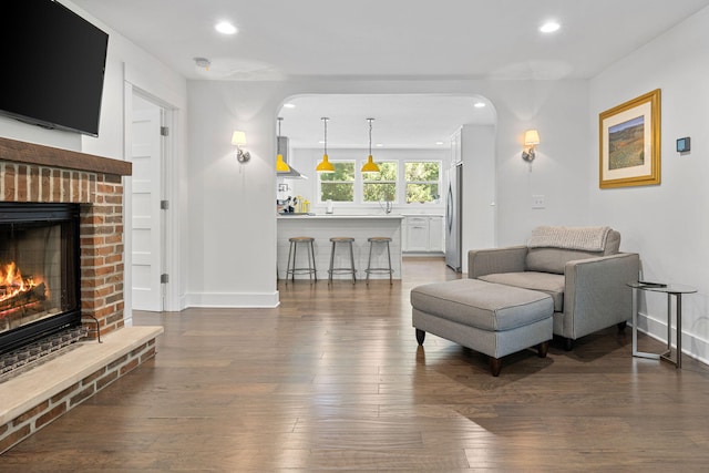 living room featuring recessed lighting, baseboards, a brick fireplace, and wood finished floors