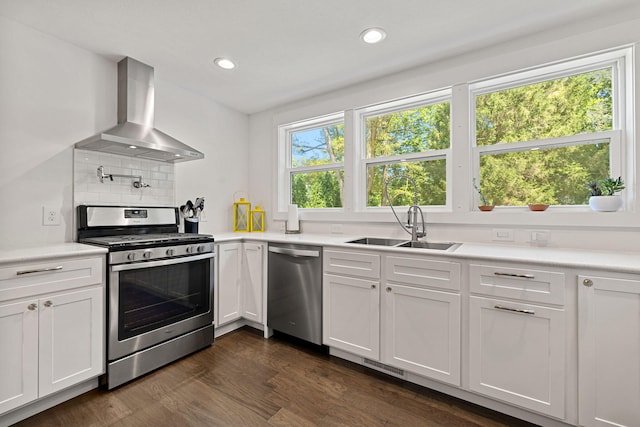 kitchen featuring wall chimney range hood, decorative backsplash, dark wood-style floors, stainless steel appliances, and a sink
