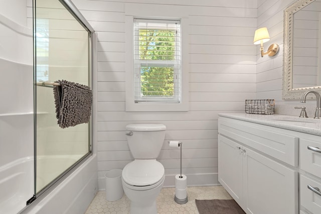 bathroom featuring tile patterned flooring, wooden walls, bath / shower combo with glass door, toilet, and vanity