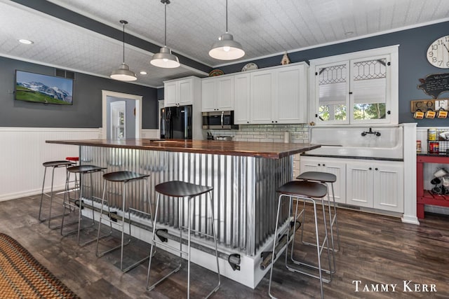 kitchen with stainless steel microwave, wooden counters, crown molding, wainscoting, and freestanding refrigerator