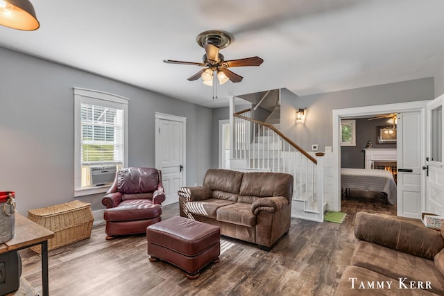 living room with ceiling fan, stairway, a lit fireplace, and wood finished floors