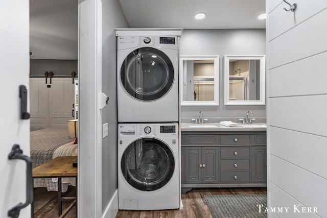 laundry room with dark wood-type flooring, a sink, a barn door, cabinet space, and stacked washer / drying machine