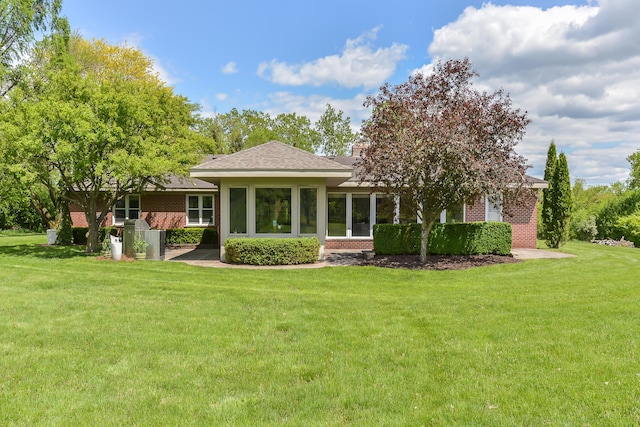 rear view of house with a yard, brick siding, and a shingled roof