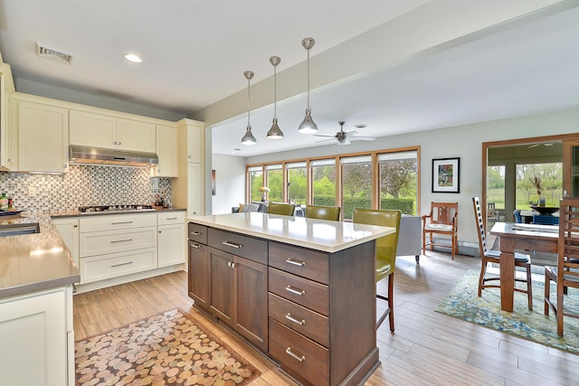 kitchen with tasteful backsplash, visible vents, under cabinet range hood, decorative light fixtures, and gas cooktop