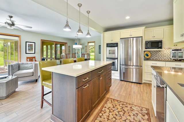 kitchen with cream cabinetry, appliances with stainless steel finishes, a breakfast bar area, decorative backsplash, and hanging light fixtures