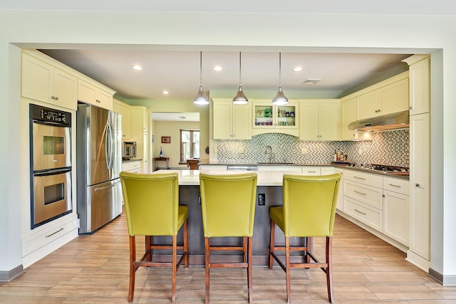 kitchen with a center island, under cabinet range hood, decorative backsplash, a kitchen breakfast bar, and stainless steel appliances