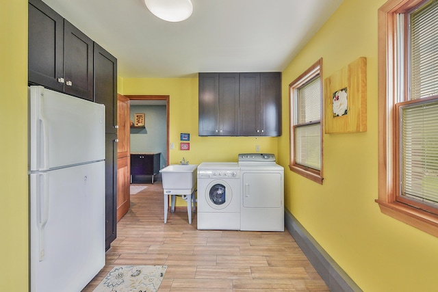 washroom with baseboards, wood tiled floor, washing machine and dryer, cabinet space, and a sink