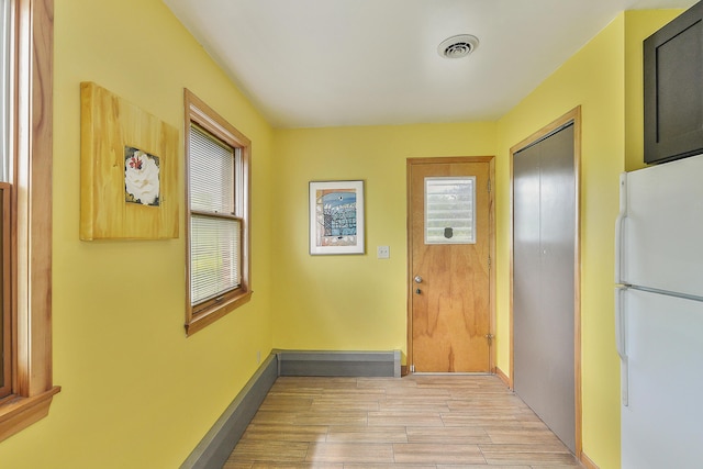 doorway with light wood-style floors, visible vents, and baseboards