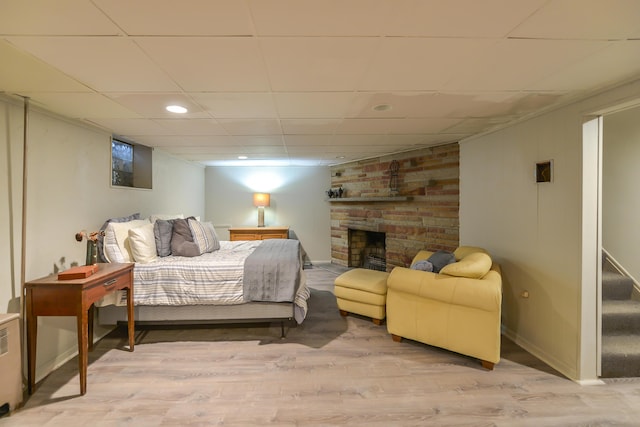 bedroom featuring a drop ceiling, wood finished floors, recessed lighting, baseboards, and a brick fireplace