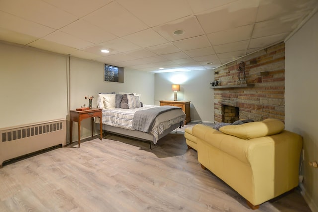 bedroom featuring a drop ceiling, wood finished floors, a large fireplace, radiator, and baseboards