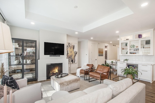 living area with beverage cooler, a glass covered fireplace, light wood-type flooring, and a raised ceiling