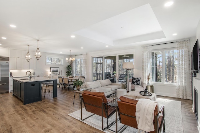 living area featuring wood finished floors, baseboards, a tray ceiling, recessed lighting, and a chandelier