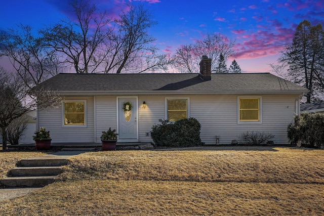 ranch-style house with a yard, a chimney, and a shingled roof