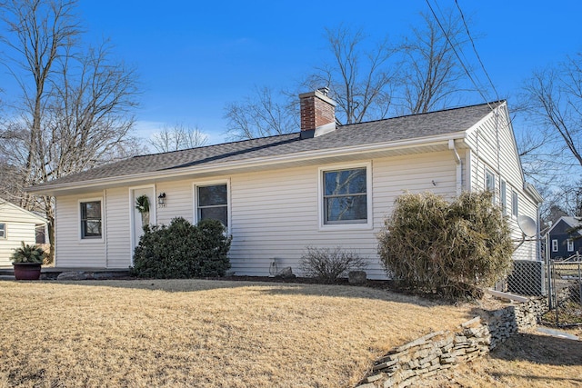 ranch-style home featuring a front yard, fence, roof with shingles, and a chimney