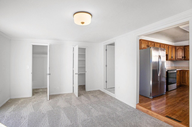 interior space with carpet floors, a walk in closet, freestanding refrigerator, and ornamental molding