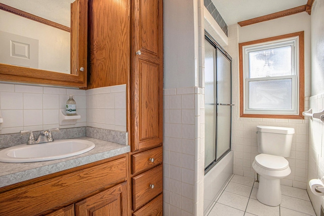 bathroom with vanity, tile patterned flooring, tile walls, toilet, and combined bath / shower with glass door