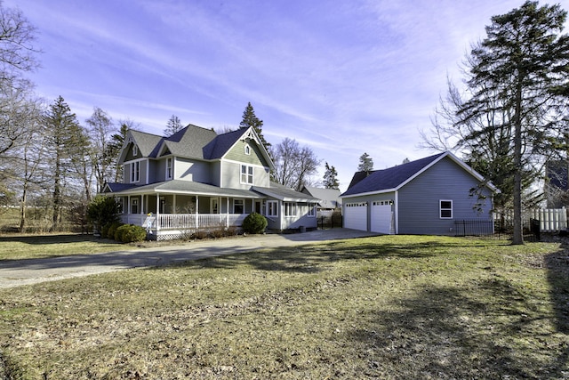 view of front facade featuring driveway, an outbuilding, covered porch, fence, and a front lawn