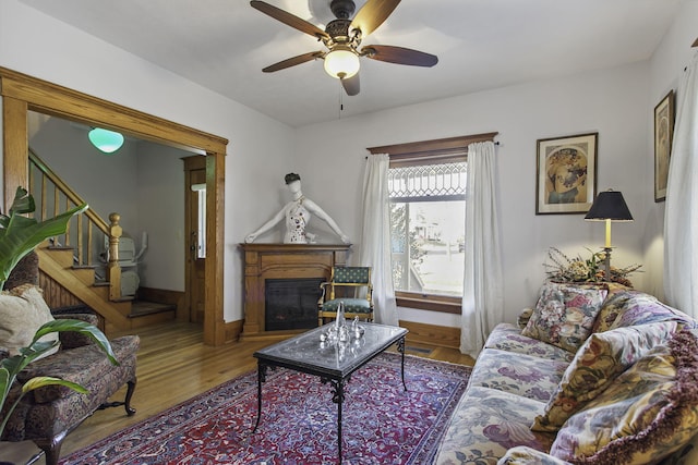 living room with wood finished floors, stairs, a glass covered fireplace, baseboards, and a ceiling fan