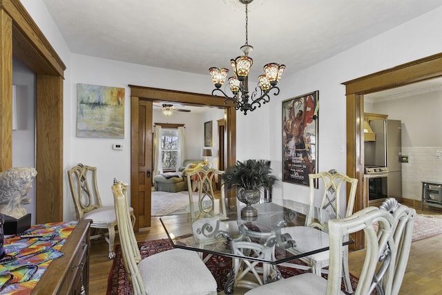 dining area with wood finished floors and ceiling fan with notable chandelier
