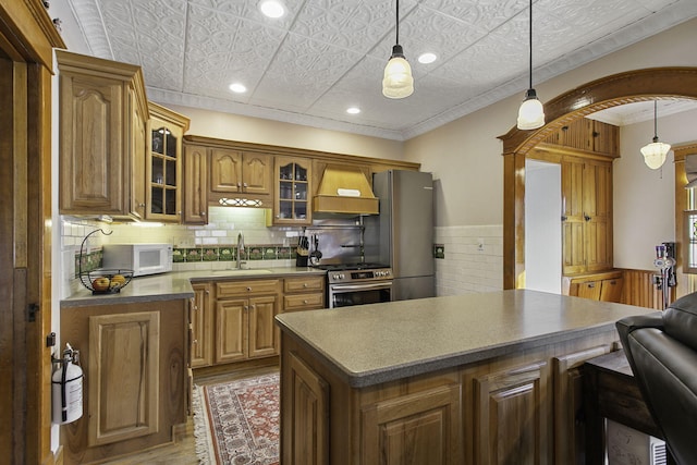 kitchen featuring a sink, glass insert cabinets, custom exhaust hood, appliances with stainless steel finishes, and wood finished floors