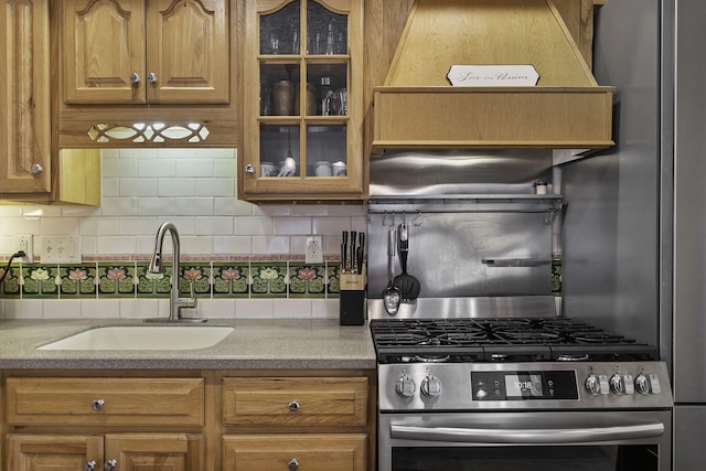 kitchen featuring a sink, glass insert cabinets, brown cabinetry, tasteful backsplash, and gas range