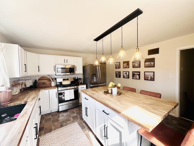 kitchen with a kitchen bar, a sink, backsplash, stainless steel appliances, and butcher block counters