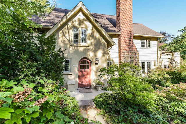 tudor-style house with a shingled roof, a chimney, and stucco siding