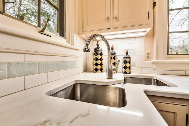 details featuring a sink, light stone counters, and backsplash