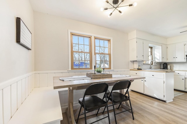 kitchen with light countertops, light wood-style floors, wainscoting, white cabinetry, and backsplash