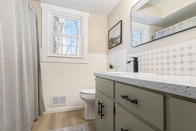 bathroom with visible vents, a wainscoted wall, toilet, wood finished floors, and vanity