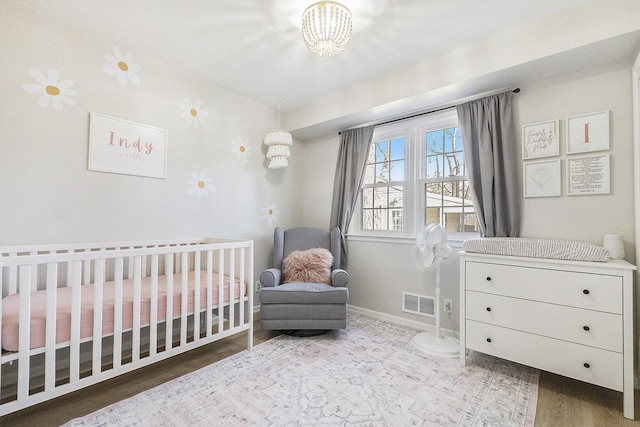 bedroom with baseboards, a crib, visible vents, and wood finished floors