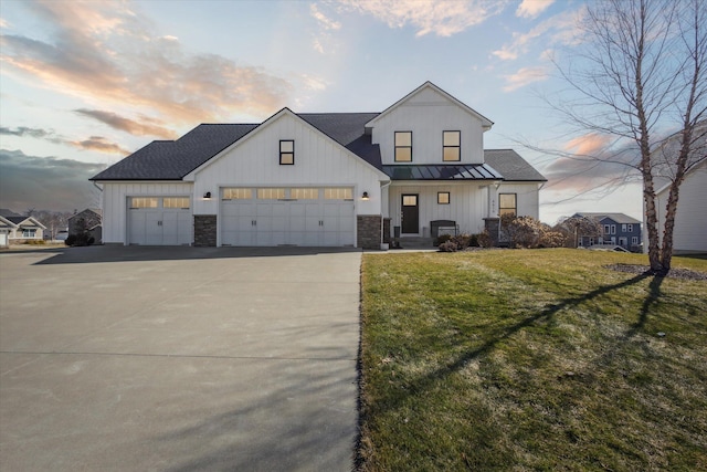 modern farmhouse style home with driveway, a standing seam roof, an attached garage, a front yard, and metal roof