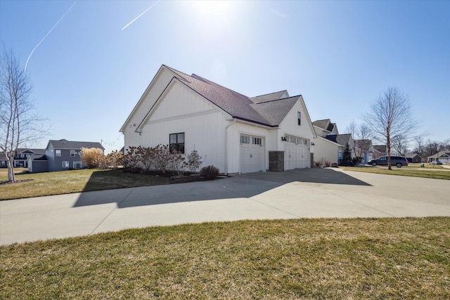 view of side of home featuring an attached garage, a yard, a residential view, concrete driveway, and board and batten siding