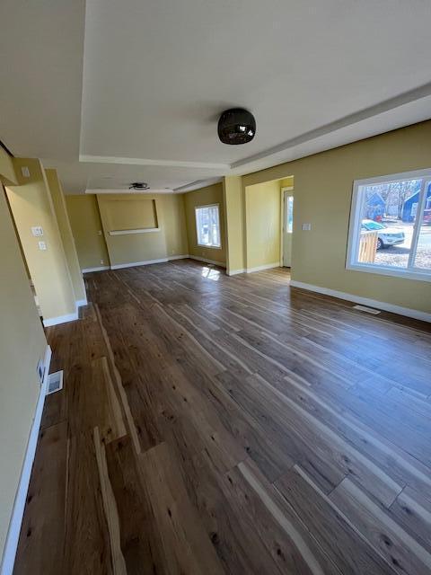 unfurnished living room featuring a wealth of natural light, visible vents, baseboards, and wood finished floors