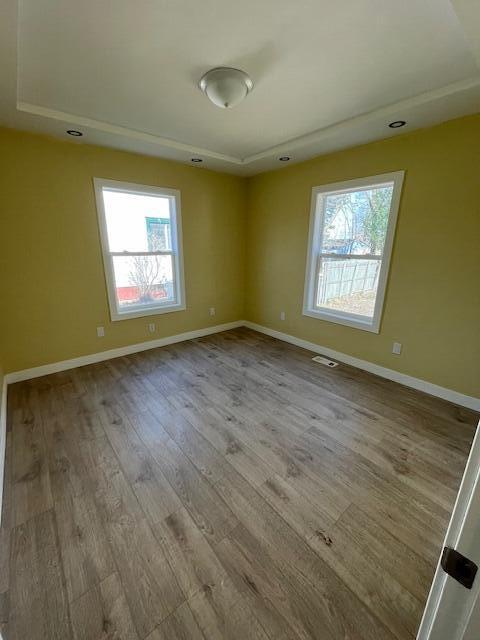 spare room with wood finished floors, visible vents, and baseboards