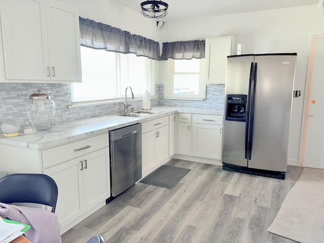 kitchen with a sink, light wood-style floors, appliances with stainless steel finishes, white cabinetry, and backsplash