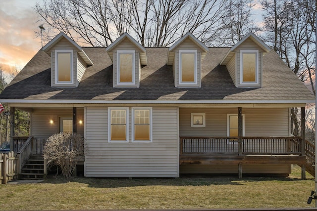 back of house at dusk with a porch, a shingled roof, and a yard