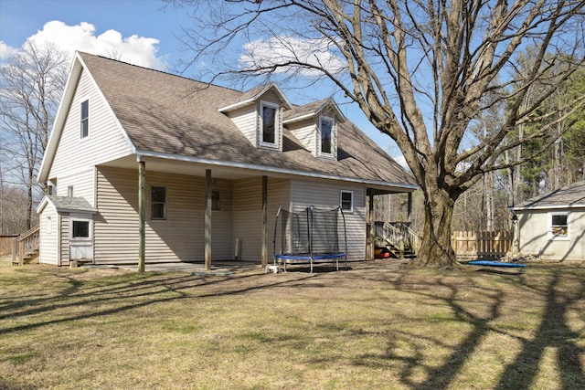 rear view of house featuring fence, a trampoline, a lawn, and a shingled roof