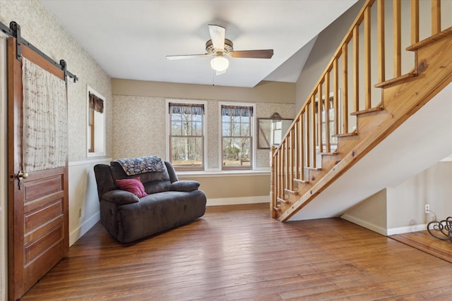 living area featuring a barn door, baseboards, hardwood / wood-style floors, and a ceiling fan