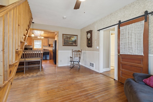 living room with visible vents, a wainscoted wall, a barn door, light wood-style floors, and wallpapered walls