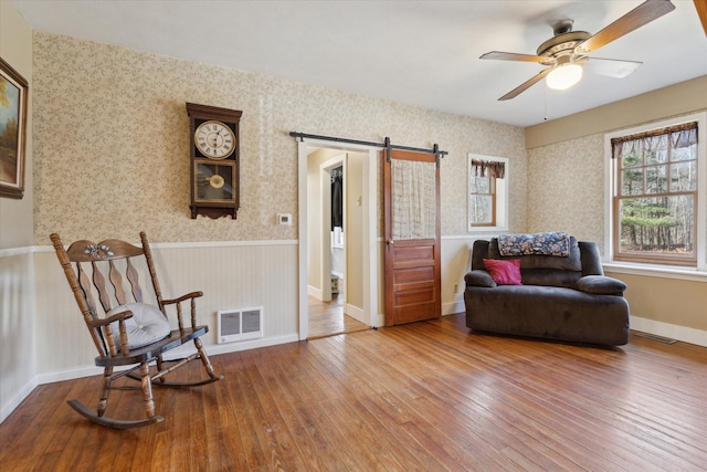 sitting room featuring wallpapered walls, a barn door, and hardwood / wood-style floors