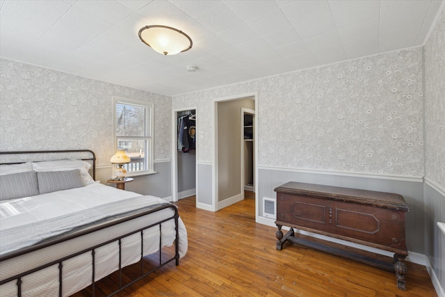 bedroom with visible vents, wallpapered walls, a closet, wood-type flooring, and wainscoting