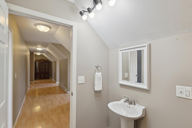 bathroom with a sink, baseboard heating, wood finished floors, and vaulted ceiling