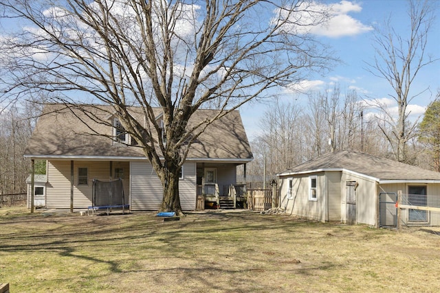 back of house featuring an outbuilding, a trampoline, a yard, and roof with shingles