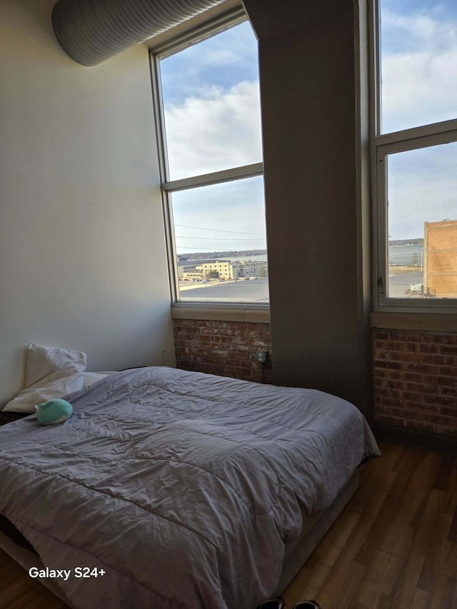 bedroom with wood finished floors and brick wall