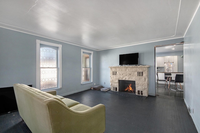 living room featuring dark wood-type flooring, ornamental molding, baseboards, and a stone fireplace